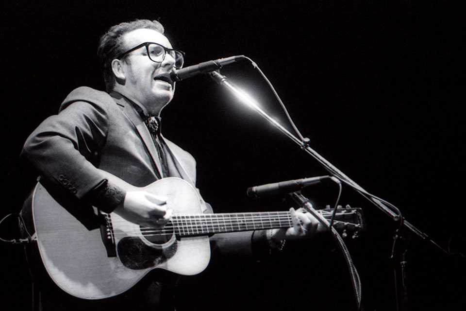 Black and white photo of Elvis Costello playing the guitar and singing into a microphone