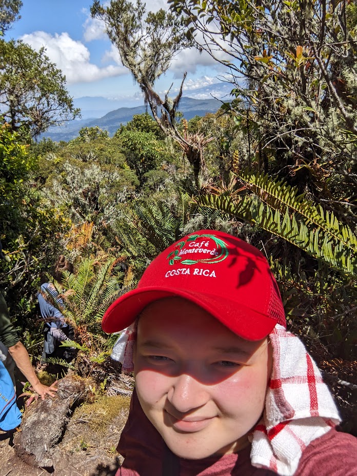 A selfie of Tyler in a red hat hiking down a mountain with other students from the program.