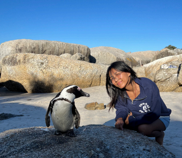 Kunga poses on the beach crouched down next to a penguin.