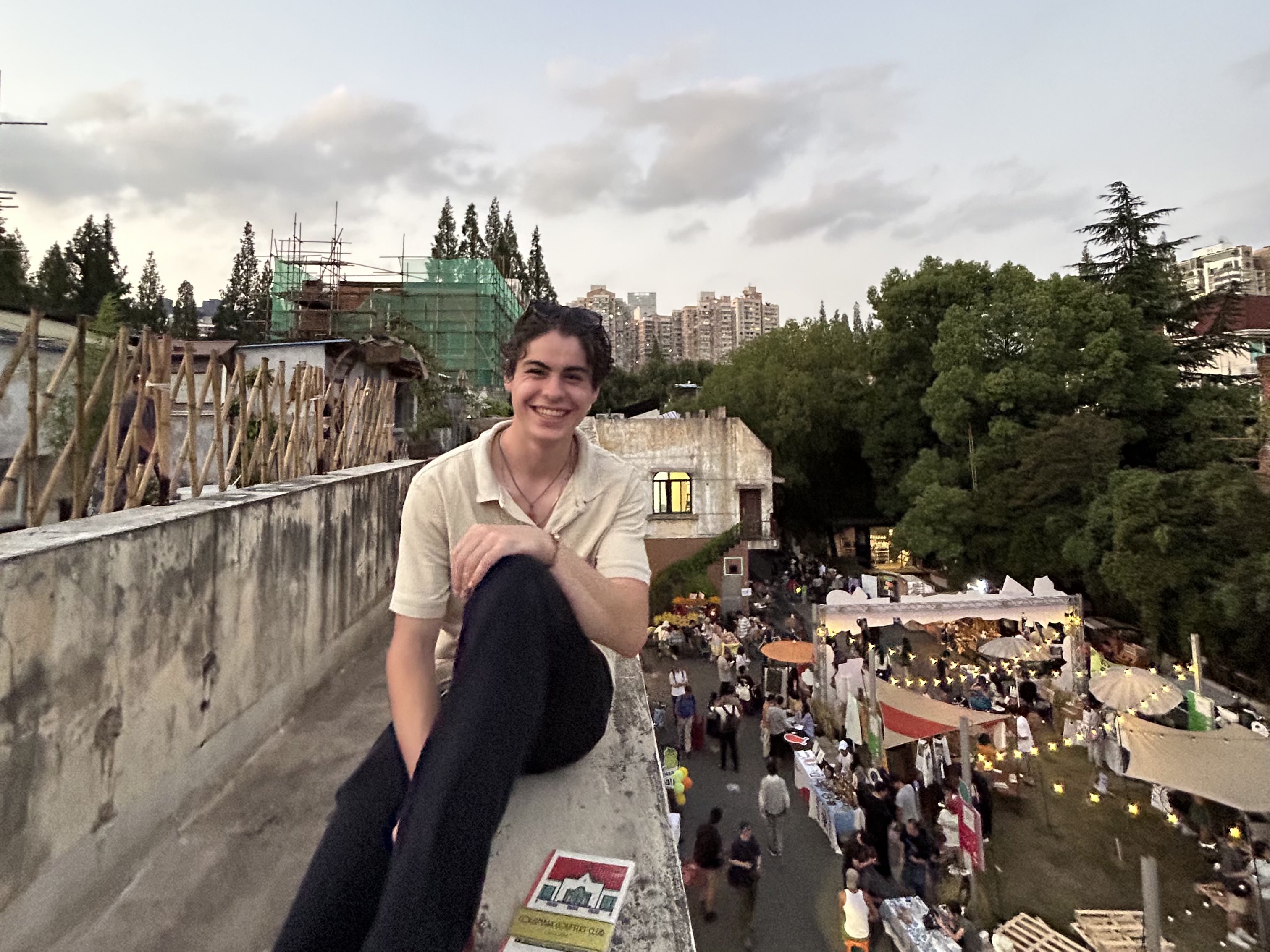 Simon sits on a wall in China with bustling streets around him.