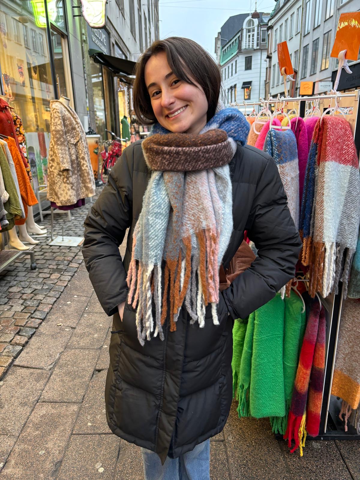 Dani stands smiling with her hands on her hips in front of a display of colorful scarves.