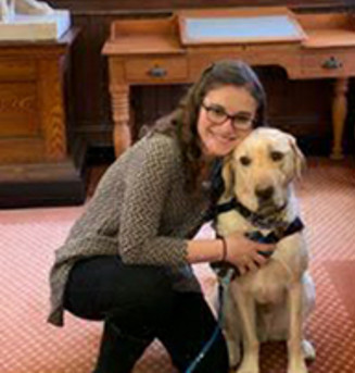 A white female with brown hair, wearing glasses and hugging a Labrador smiling into the picture