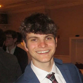 A headshot of David. A male with brown hair wearing a blue suit jacket and a red and gray tie.