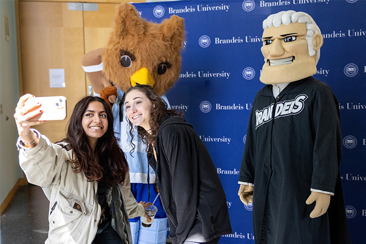 Two students taking a selfie with the owl mascot, with the judge mascot standing to the side