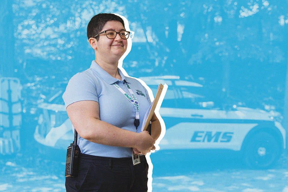 A woman holding a clipboard stands in front of an EMS vehicle.