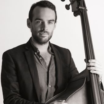 James has short dark hair and wears a suit. He holds a cello.