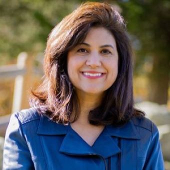 Marjan has wavy brown hair and wears a blue blouse.