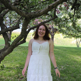 Eleanor Flynn has long brown hair and wears a white sundress.