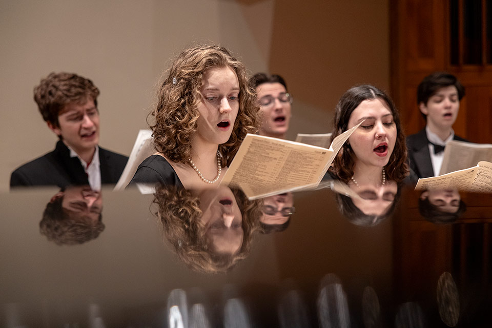 Five people singing on stage while holding sheet music