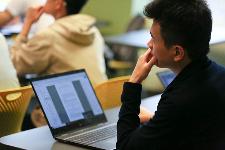 A student on a laptop looks up with their chin in their hand