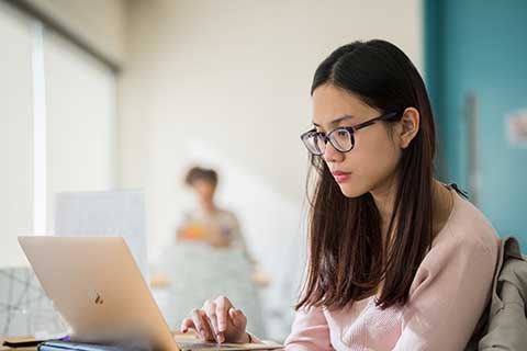 a student wearing glasses looks a a laptop
