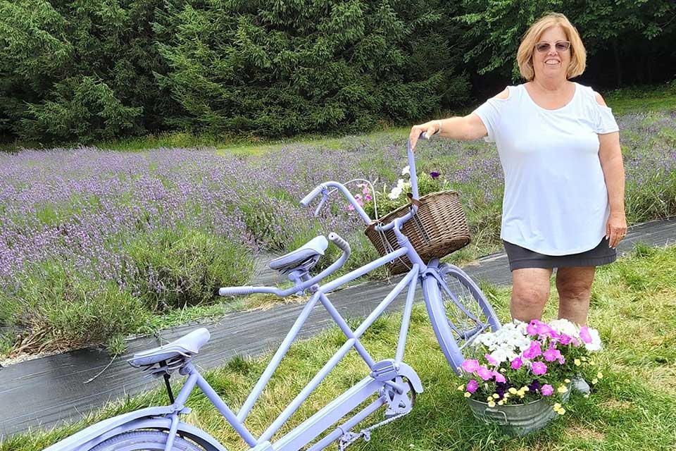 Woman stands outside next to colorful bicycle and flowers