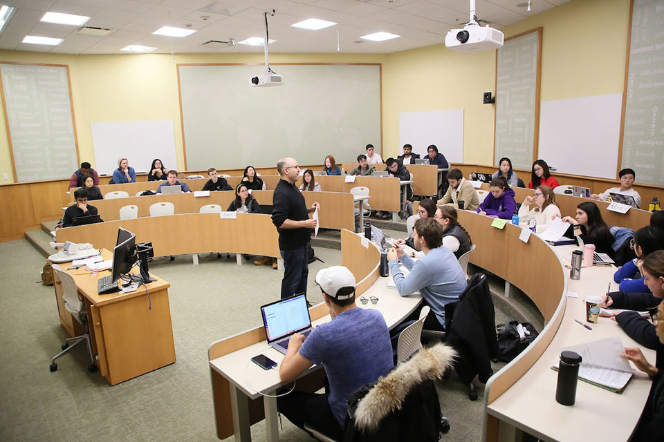 A professor speaks to a room full of students in a lecture hall.