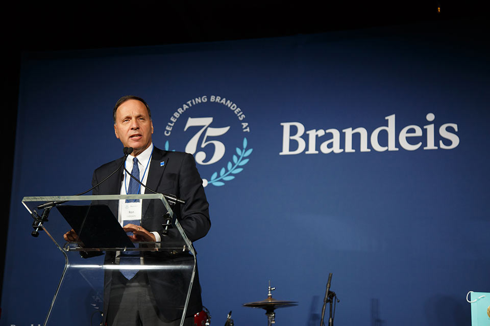 Ron Liebowitz speaking at a podium, the Brandeis logo appears in the background