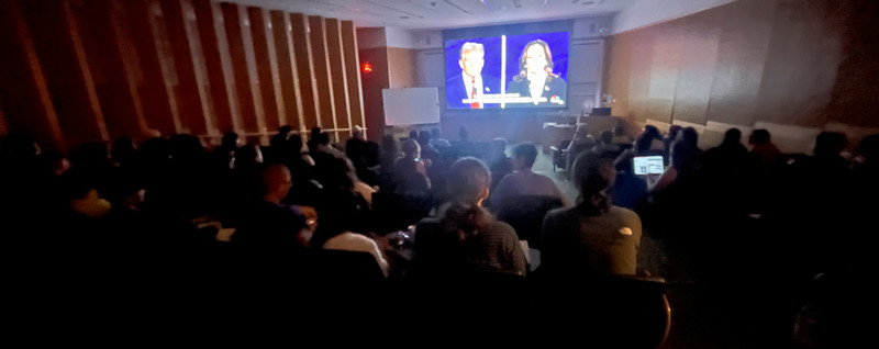 audience in classroom watching presidential debate on big screen