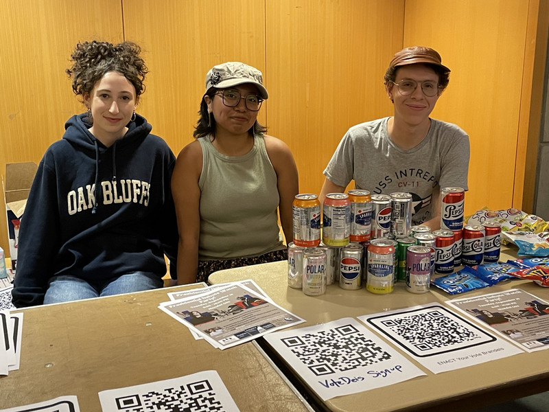 Three studest sit behind a voter registration table smiling