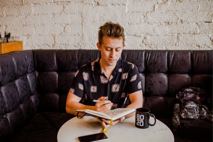 Person looking at a laptop with pen and notebook in hand