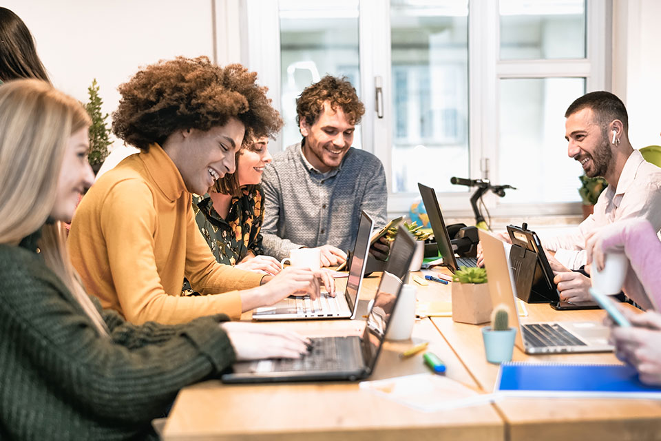 A group of people sit smiling around a table on their computers.