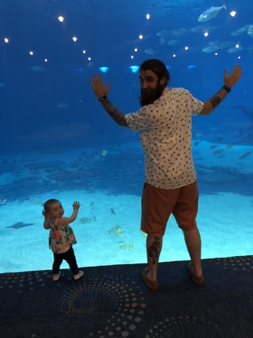 Dominic Lombardi standing in front of an aquarium tank with a toddler standing beside him.