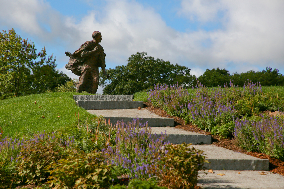 The Louis Brandeis statue on the Brandeis campus. Steps lead up to the statue, which is surrounded by grass and flowers.