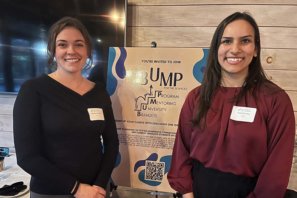 Camille Sullivan and Anjali Pandey stand in front of a poster with the Brandeis University Mentoring Program logo.