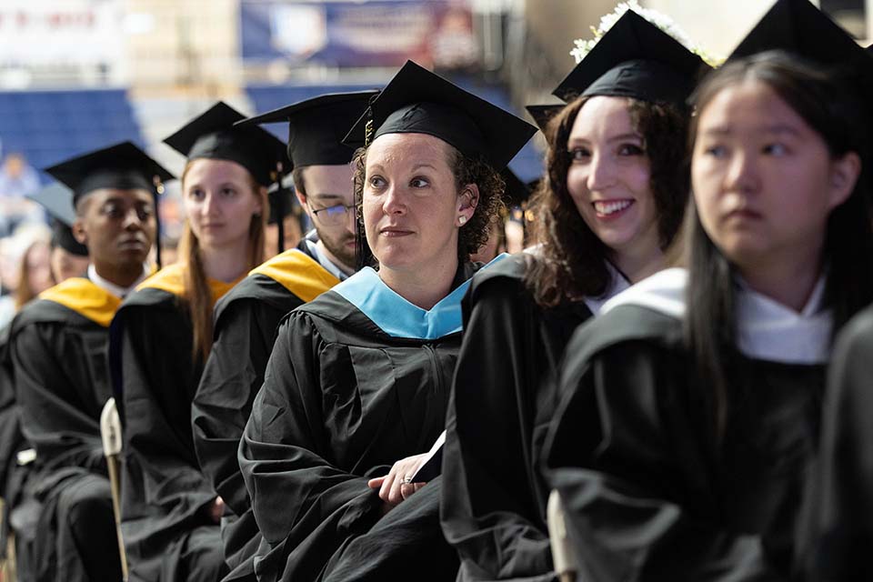 Graduates in caps and gowns sit in rows of chairs.