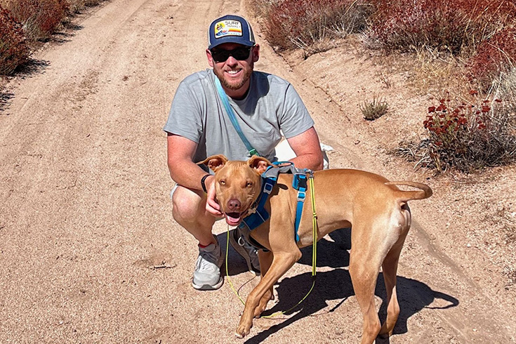 Jorah Dannenberg squats on a trail with a dog in front of him.