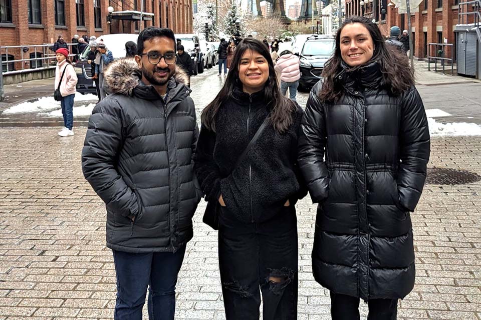 Sayan Biswas, Jazmin Morales, and Marissa Ashton stand in a row in Brooklyn's DUMBO neighborhood, wearing winter coats.