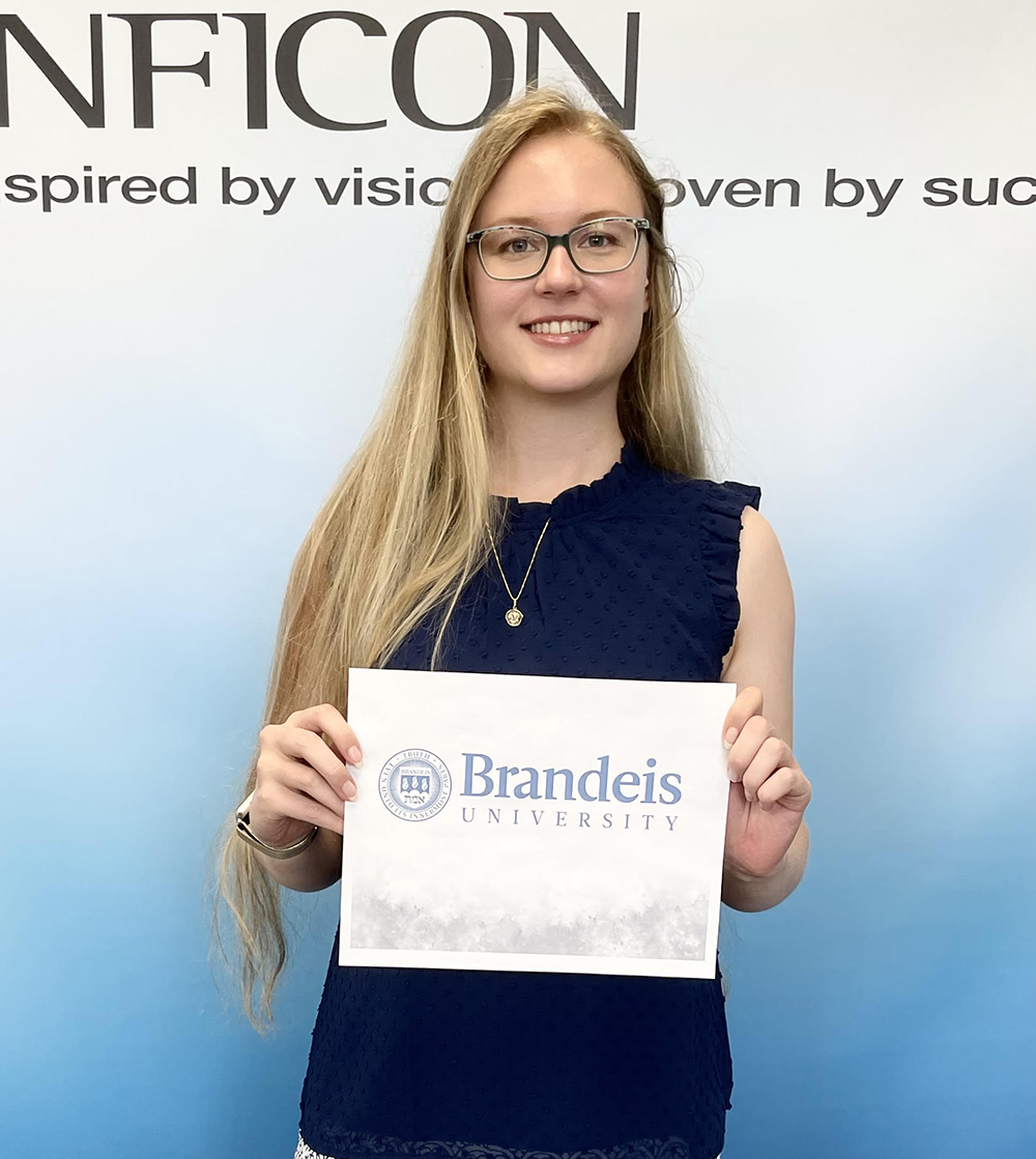 Annika Sparrell standing in front of an Inficon backdrop, holding a paper that says "Brandeis University"