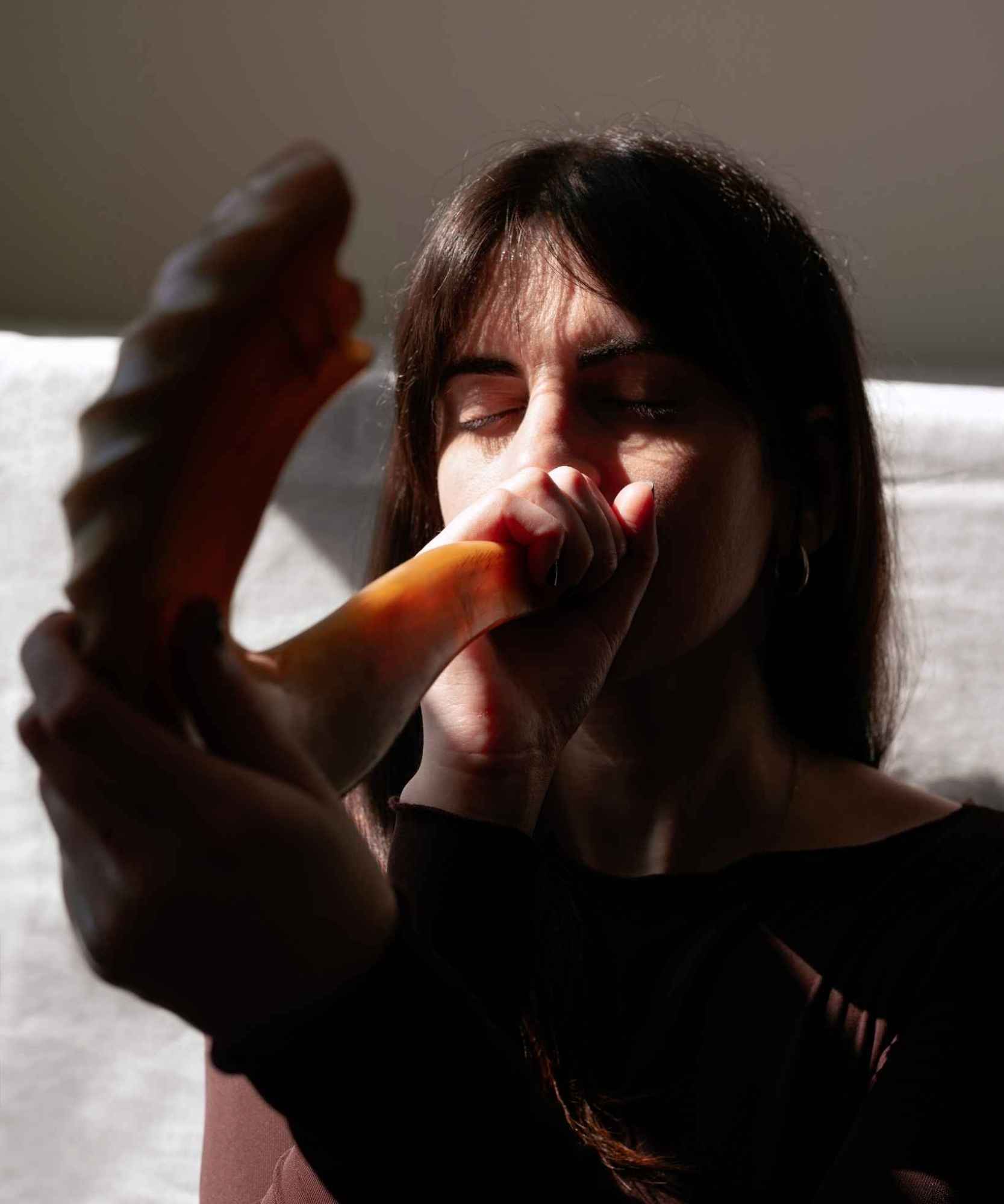 A woman with closed eyes holding a shofar to her mouth and her hand closed around the shofar opening