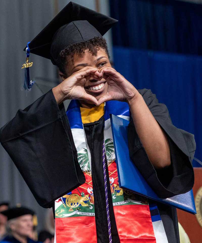 Brandeis University student speaker Nathalie Vieux-Gresham makes the shape of a heart to her fellow graduates after walking across the stage during the undergraduate Commencement ceremony at the Gosman Sports and Convocation Center.