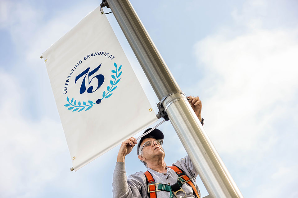 A Brandeis staff member installs a Brandeis 75 Anniversary banner on campus.