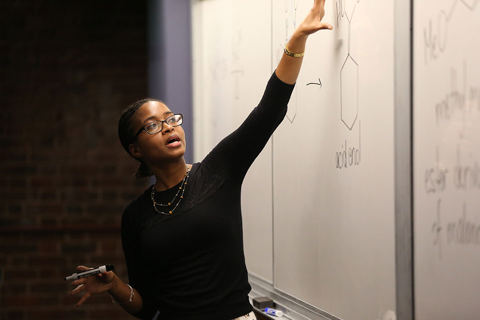 A professor gives a lecture and points at a whiteboard.