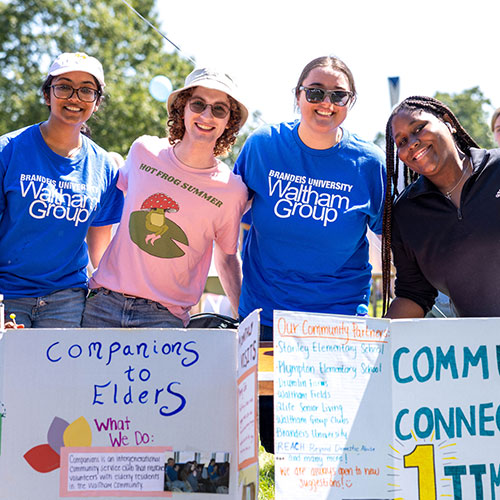 Four students stand next to signs at the Brandeis involvement fair.