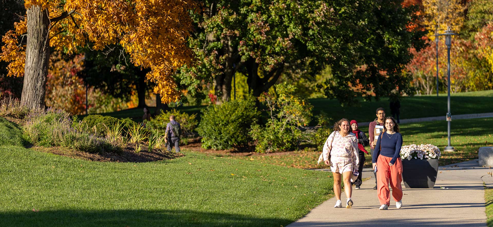 Two students sitting in chairs on the Brandeis campus, fall colors surrounding them