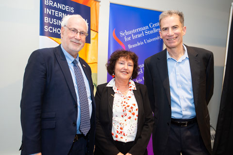 Ambassador Zeev Boker, Consul General of Israel to New England, keynote speaker Karnit Flug, and conversant Gideon Argov posed, smiling, in front of multi-colored banners for the Brandeis International Business School, and the Schusterman Center for Israel Studies at Brandeis University.