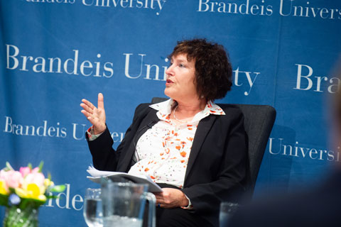 Woman, Karnit Flug, seated on stage, speaking, gesturing with an open hand as she makes a point. 