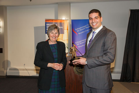 Tall young man stands holding an award shed like a miniature of the Louis Brandeis sculpture on the Brandeis University campus, while Brandeis International Business School Dean Kathryn Graddy stands to his left, having just handed him the award. 