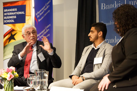 Older man gestures as he speaks to younger man and younger woman as the three sit onstage during a panel discussion.