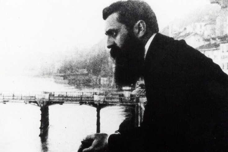 Black and white image of Herzl leaning on a balcony rail in contemplation over a body of water