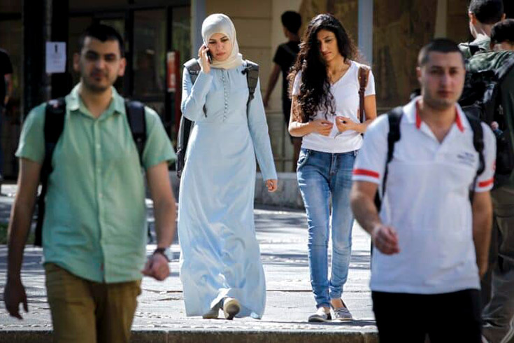 young people with backpacks walking outdoors, among them, a young woman in a hijab 