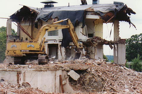 An excavator clears away debris while sitting on the second floor. The boulder is at the bottom of the photograph.