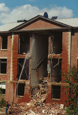 Close up of the front of Ford Hall after wrecking crew tore down the central section.  A hose sprays the building. A pile of rubble on the ground in front.
