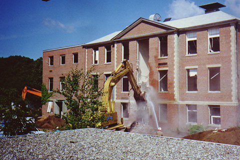 Members of the crew using hoses to keep the dust down while the crane continues to tear down the front of Ford Hall.