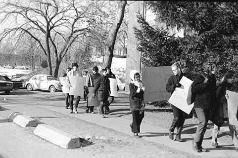 White students holding paper signs and walking in a line around a building.