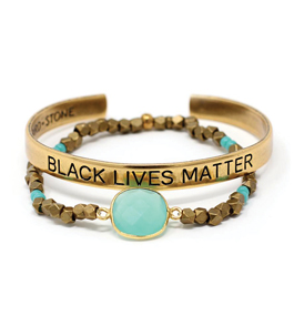 Photo of two bracelets. One is gold-colored, engraved with "Black Lives Matter." The other features a large central turquoise-color stone flanked by metal and blue-stone beads.