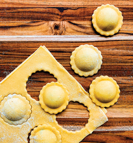 Photo of ravioli cut out of a sheet of pasta by a round cutter with a fluted edge.
