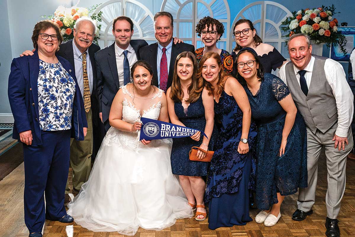 A wedding party poses for a photo while holding a Brandeis flag.