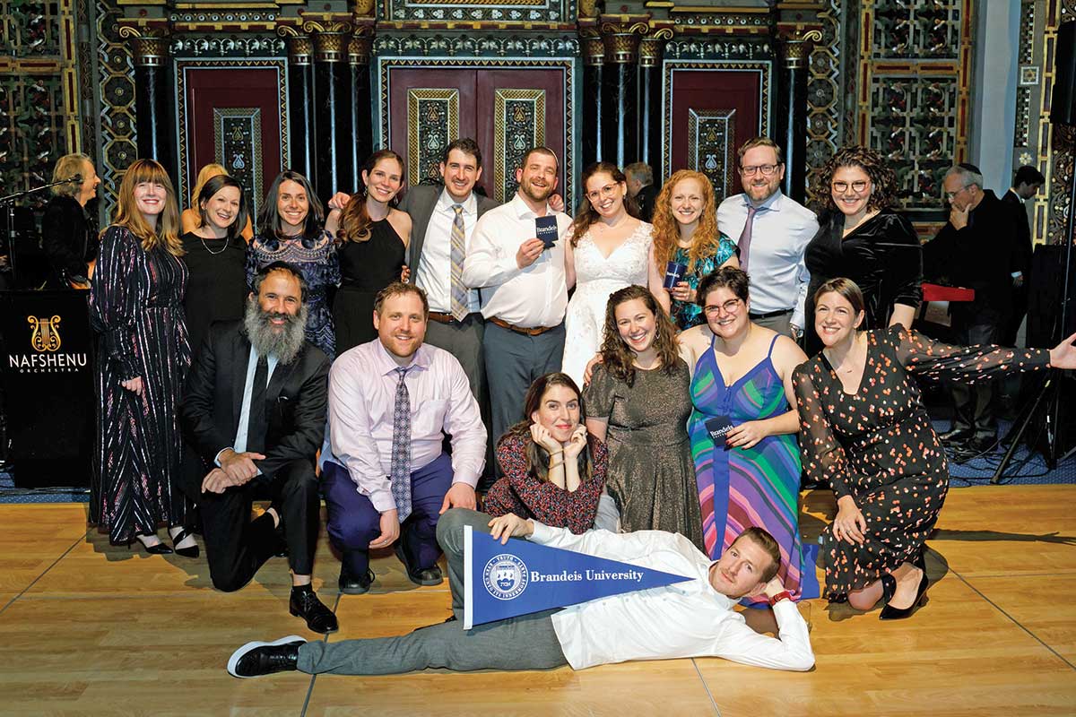 A group of people pose with a Brandeis flag at a wedding.