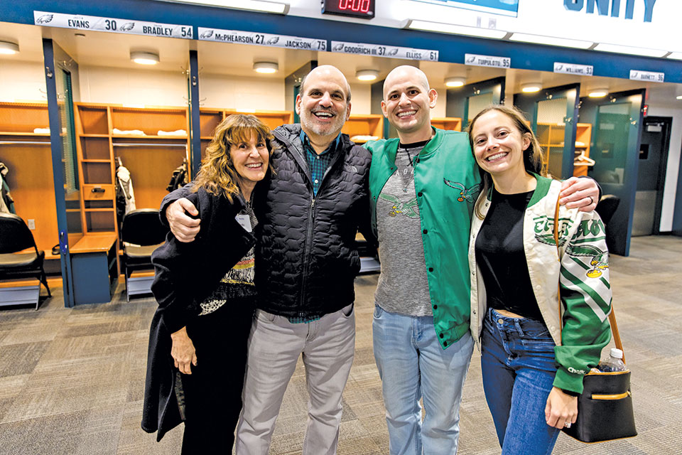 Four alumni pose together in the Philadelphia Eagles' locker room.
